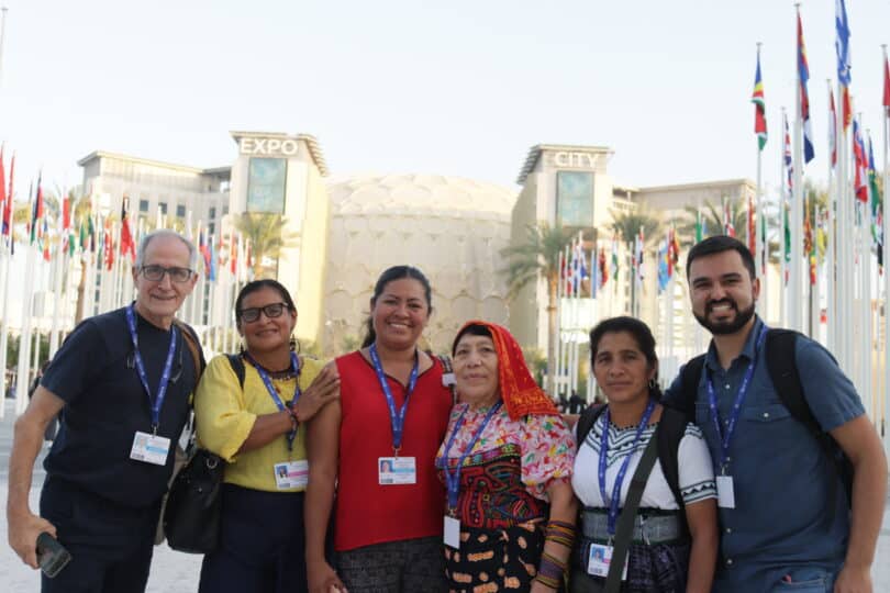 A group of COP delegates in Dubai stand in a row smiling at the camera.
